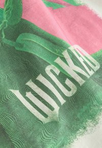 Bomullstyg med en djärv grön och rosa grafisk design med texten "WICKED" i stora, vita bokstäver, som visar en slät yta.
