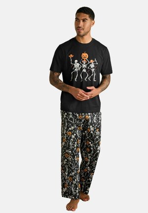 Black cotton t-shirt featuring skeletons with Halloween accents. Paired with black pajama pants adorned with orange pumpkins and skeleton patterns.