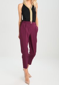 Svart ärmlös topp med en guldskimrande V-ringning; matchad med vinröda skräddarsydda byxor med en knapp i fram och vecket. Beige högklackade skor.