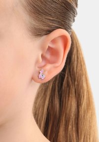 Pendientes de stud en forma de llama rosa con acentos coloridos, enmarcados en la oreja de un modelo, destacando el diseño metálico y el detalle juguetón.
