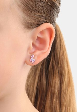 Pendientes de stud en forma de llama rosa con acentos coloridos, enmarcados en la oreja de un modelo, destacando el diseño metálico y el detalle juguetón.