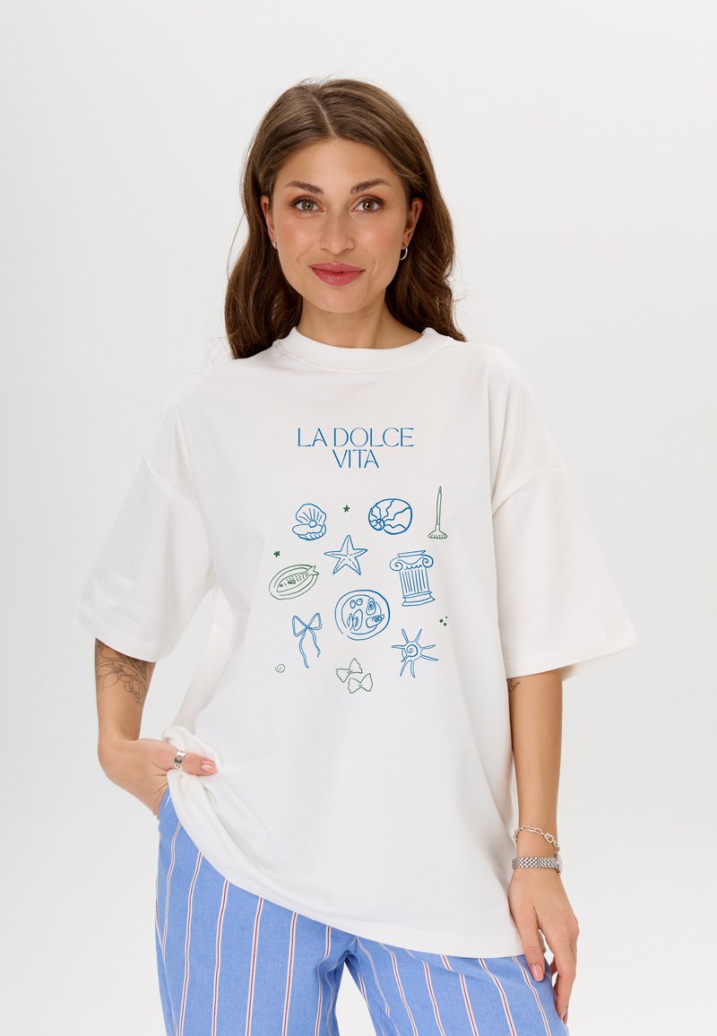 Witte oversized t-shirt met een blauw en groen geïllustreerd ontwerp met schelpen, sterren en een zuil. Zacht materiaal, relaxed fit.