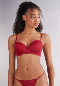 Rotes Spitzen-Lingerie-Set mit gepolstertem BH und gewelltem Rand sowie passendem Tanga. Filigrane geometrische Muster zieren den Stoff.