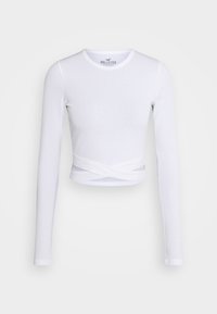 Vit ribbade långärmad topp med kortad design och korsad frontdetalj. Tillverkad av ett mjukt, elastiskt material.