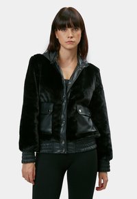 Sort faux fur og læder bomberjakke med trykknapper, to forlommer, ribbede manchetter og en stylet krave. Glat tekstur og rent design.
