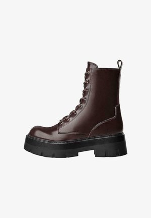 Smeđe kožne gležnjače s vezanjem sprijeda, okruglim nosom i debelim crnim platformama. Ima povlačenje na leđima. Glatka tekstura.