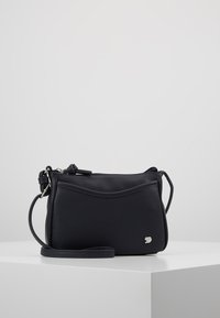 Geantă mică neagră de tip crossbody cu logo argintiu de animal, închidere cu fermoar și curea reglabilă, expusă pe o suprafață albă cu fundal simplu.