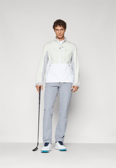 Light gray zip-up jacket with white accents, paired with light gray pants and white shoes featuring blue soles. Golf club in hand.
