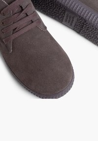 Chaussure en daim marron avec un nez arrondi et une semelle en caoutchouc texturé. Dispose de lacets et de coutures assortis pour un design homogène.