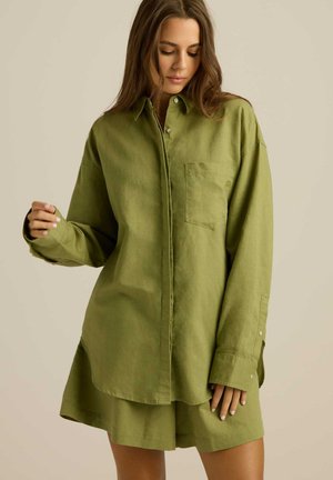 Olśniewająca oliwkowo-zielona lniana koszula z wygiętym kołnierzykiem, z guzikami z przodu, jedną kieszenią na piersi i długimi rękawami. Miękka tekstura i luźny krój.