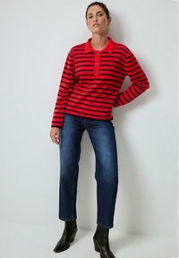 Röd och marinrandig långärmad polo med tre knappar, parat med raka blåjeans och svarta ankelboots. Slät, figursydd tyg.