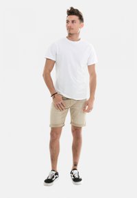 T-shirt blanc à manches courtes associé à un short beige avec un ourlet roulé. Des baskets noires et blanches complètent le look décontracté.