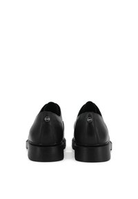 Scarpe in pelle nera con finitura liscia, punta arrotondata, tacco leggero e suola in gomma texturizzata. Accento in metallo sul retro.