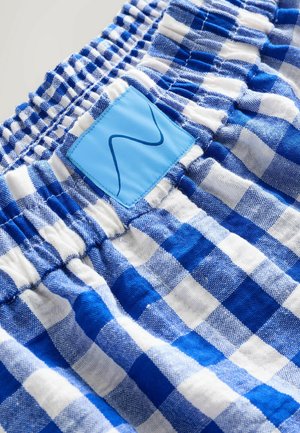 Blåt og hvidt ternet stof med elastisk taljebånd og en lyseblå lap med en mørkeblå bølget linje.