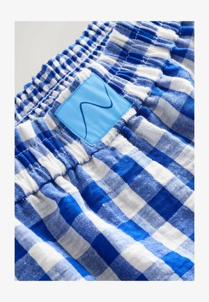 Blåt og hvidt ternet stof med elastisk taljebånd og en lyseblå lap med en mørkeblå bølget linje.