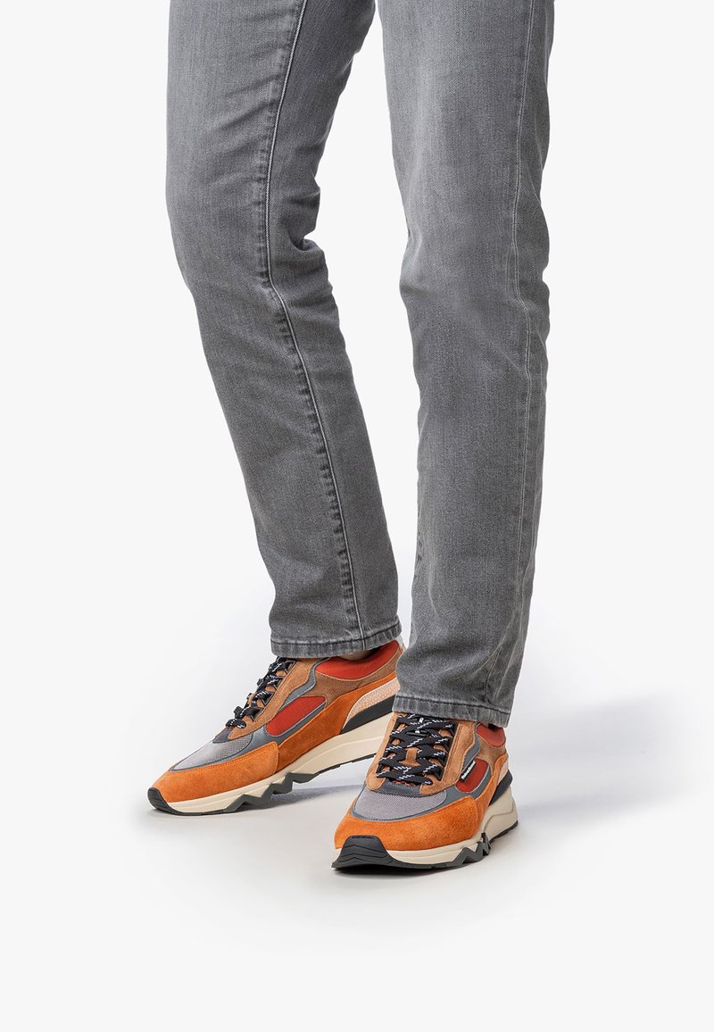 Scarpe sportive arancioni e grigie realizzate con materiali misti, caratterizzate da una tomaia testurizzata, allacciatura prominente e una suola spessa in stile blocco.