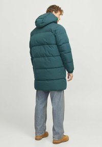 Teal jakna od pufastog materijala s kapuljačom, te quilted dizajnom i dugom dužinom. Uparena s svijetloplavim trapericama i smešnim cipelama.