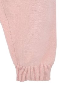 Manica di un maglione rosa lavorato a maglia, con un polsino a costine e una texture liscia. Il design è semplice, senza motivi o decorazioni visibili.