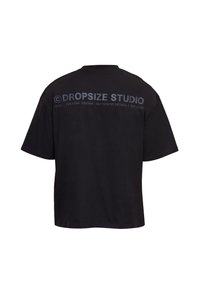 T-shirt noir oversize à manches courtes, avec l'inscription "DROPSIZE STUDIO" et un slogan imprimés sur le haut du dos.