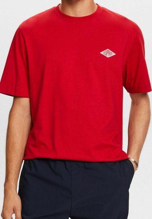 Rotes T-Shirt mit kurzen Ärmeln aus Baumwolle. Verfügt über ein kleines weißes Grafiklogo auf der linken Brust. Klassisches Rundhalsdesign.