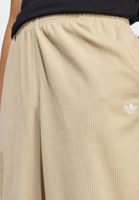 Beige corduroy sweatpants with an elastic waistband and subtle, white embroidered logo. The fabric features vertical ribbed texture.