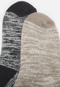 To sæt sokker; det ene i sort og gråt meleret mønster, det andet i lys beige med en ribbet tekstur. Begge har rundede tæer.