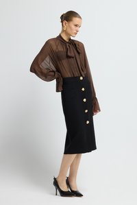 Hnědá průsvitná halenka s límečkem na mašličku, doplněná černou kolovou sukni ke kolenům s detaily zlatých knoflíků a kapsami.