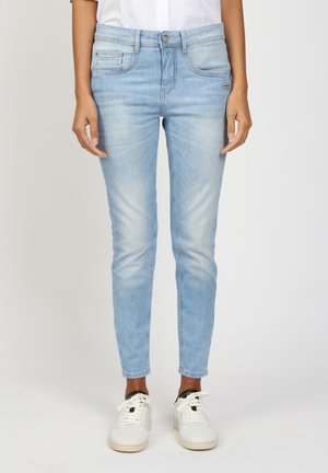 Slim-fit light blue jeans with faded detailing worn with white sneakers and a white shirt, shown from waist to feet.