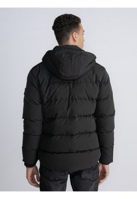 Abrigo puffer negro con capucha, que presenta un diseño acolchado y puños acanalados. La tela parece suave con un acabado mate.