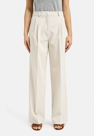 Beige wide-leg trousers in a textured fabric with pleats and a tailored waistband. Worn with brown strappy sandals.