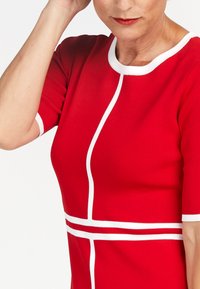 Abito rosso aderente con maniche corte, caratterizzato da righe orizzontali e verticali bianche. Tessuto liscio con scollatura rotonda.