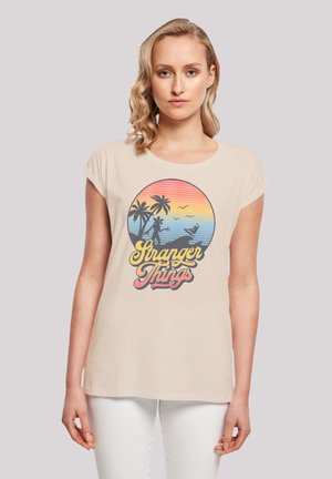 Beige T-Shirt mit kurzen Ärmeln, das ein farbenfrohes Grafikdesign von Palmen und einem Sonnenuntergang zeigt, mit dem Text "Stranger Things" in fetter, stilisierter Schrift.