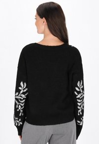Czarny sweter wykonany z dzianiny, z białymi cekinowymi wzorami w kształcie liści na rękawach oraz luźnym dekoltem. Miękka tekstura i dopasowanie.