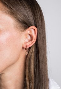 Orecchini a cerchio in tono dorato con un piccolo ciondolo a forma di cuore, decorato con un motivo a perline, che mette in risalto una superficie lucida e un design delicato.
