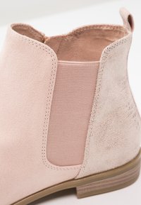 Gros plan d'une bottine rose pâle avec panneau latéral élastique, dos texturé, détails cousus et petit talon en bois.