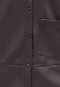 Mörkbrun läderjacka med knappstängning fram, en bröstficka och rena sömmar för en figursydd look. Slät, matt yta.