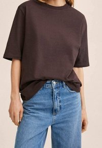 Mørkebrun T-shirt med korte ærmer lavet af bomuld, med rund halsudskæring og en afslappet pasform, parret med lyseblå højtaljede jeans.
