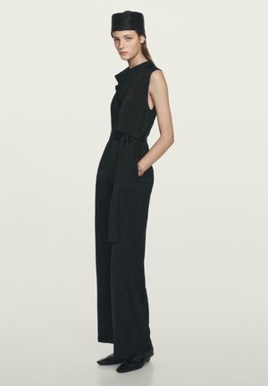 Black jumpsuit with wide legs, sleeveless design, belted waist, and a rounded collar. Complemented by a textured black hat.