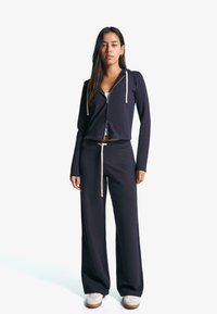 Navy zip-up kort hoodie med vita dragsko tillsammans med matchande vida sweatpants och ljusa sneakers, med en avslappnad passform.