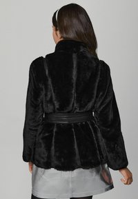 Schwarze Kunstfelljacke mit tailliertem Schnitt, kragenförmigem Design und langen Ärmeln. Glatte Textur mit einem subtilen Schimmer. Silberner metallic Rock.