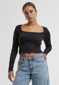 Svart langermet crop topp med firkantet utringning, laget av glatt stoff. Sammen med høy midje lyseblå denimjeans.