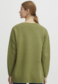 Pull en maille vert avec un motif texturé, à manches longues et coupe ample, présentant un large col et des épaules tombantes.