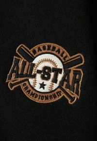 Un tissu noir présente un patch brodé avec "ALL-STAR" au-dessus d'un baseball et de crosses de batte, accentué en fils marron et crème.