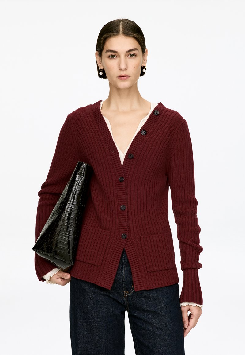 Burgundy ribbed cardigan with v-neck, front pockets, and black button closures, paired with a black faux-crocodile handbag.
