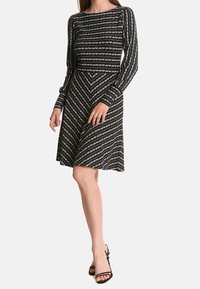 Schwarz-weißes Langarmkleid mit einem Zickzackmuster, einem taillierten Oberteil und einem ausgestellten Rock, hergestellt aus weichem Stoff.