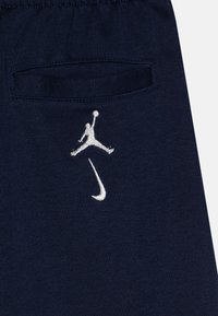Navy blue fabric joggers featuring a white embroidered Jumpman logo above a small pocket and a curved Nike swoosh design.