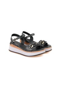 Zwarte leren platform sandalen met enkelbandjes, voorzien van gouden hardware en een gestructureerde zwarte kettingaccent. Witte en tan zool.