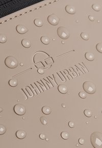 Gros plan de gouttes d'eau sur une surface beige embossée d'un logo et du texte « JOHNNY URBAN ».