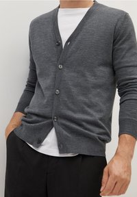 Graue Strickstrickjacke mit V-Ausschnitt, sechs Knöpfen und langen Ärmeln. Weiche Textur, lässiges Design, kombiniert mit einem weißen T-Shirt.