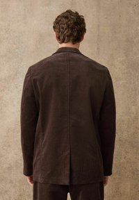 Hnědý kordový blazer s dobře padnoucím střihem. Obsahuje vertikální žebrování, klopový límec a jeden roz ventu vzadu. Jednoduchý, čistý design.